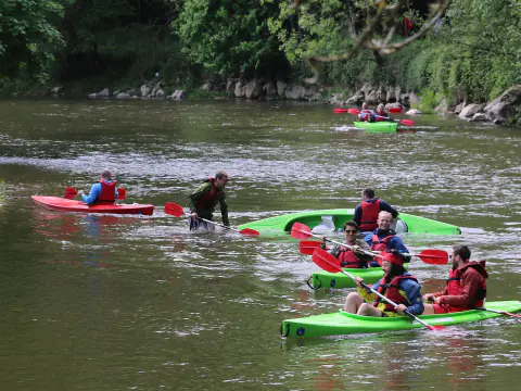 Groupe de kayaks colorés qui descendent la Lesse en Ardenne belge, entre berges boisées