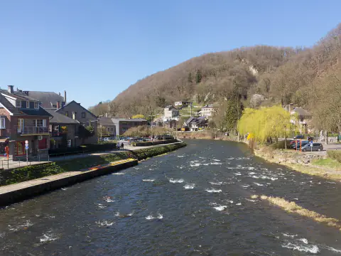 L'Amblève à Aywaille, avec de petits rapides devant des maisons et une colline boisée